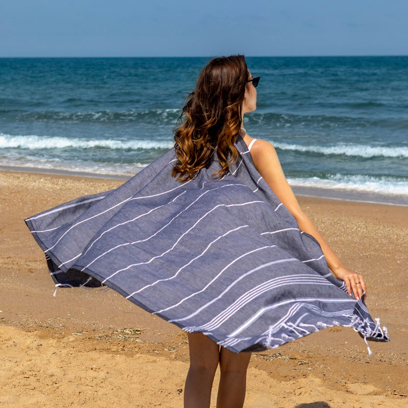 Femme utilisant une serviette fouta écologique sur la plage, symbolisant les avantages écologiques des serviettes fouta